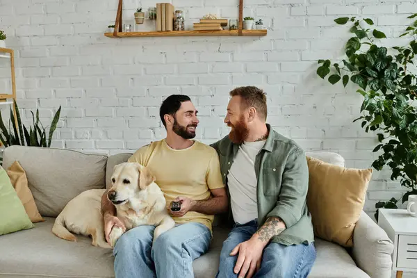 Two men with beards cuddling a Labrador on a comfortable couch in a living room. — Stock Photo