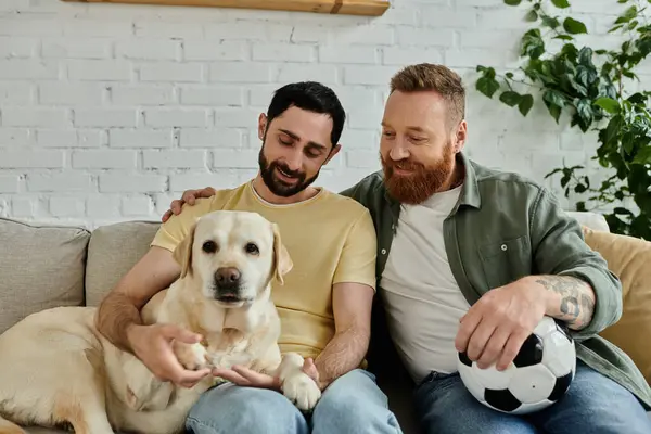 Bearded gay couple cuddle with their labrador on a cozy couch in their living room, sharing a moment of tranquility. — Stock Photo