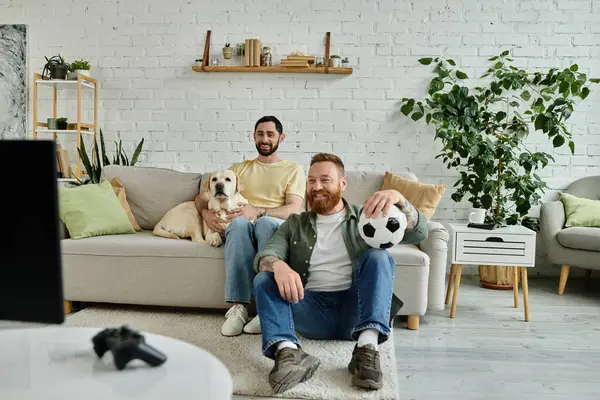 A bearded man sits on a couch, holding a soccer ball, deep in thought, while spending quality time in the living room. — Stock Photo