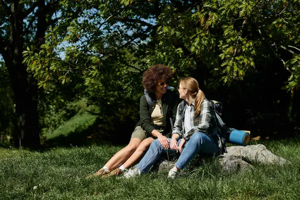 Una giovane coppia lesbica multiculturale si siede insieme su una roccia nel bosco, godendosi una pausa dalla loro escursione. — Foto stock