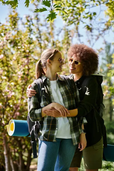 Una joven pareja lesbiana multicultural camina por el bosque en un día soleado, compartiendo un abrazo amoroso. - foto de stock