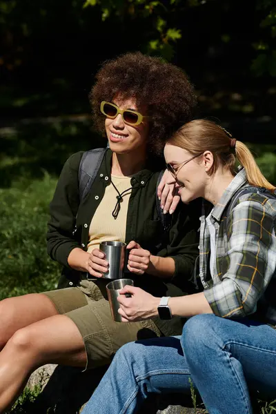 A young lesbian couple hikes in the wilderness, enjoying a moment of rest and sharing a cup of coffee. — Stock Photo