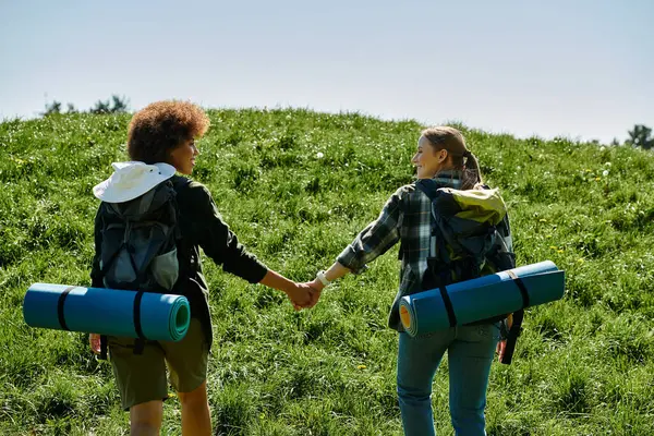A young, multicultural lesbian couple hikes through a grassy field, holding hands and enjoying their time in nature. — Stock Photo