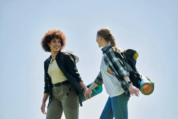 Dos mujeres jóvenes, una pareja de lesbianas, caminan juntas en el desierto, disfrutando del aire libre. - foto de stock