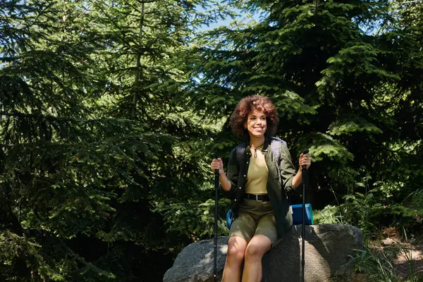 A young woman enjoys a break during her hike, sitting on a rock in a lush forest, surrounded by towering trees. — Stock Photo