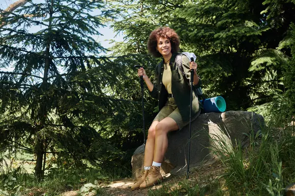 A young woman takes a break during her hike, sitting on a rock in the woods. — Stock Photo