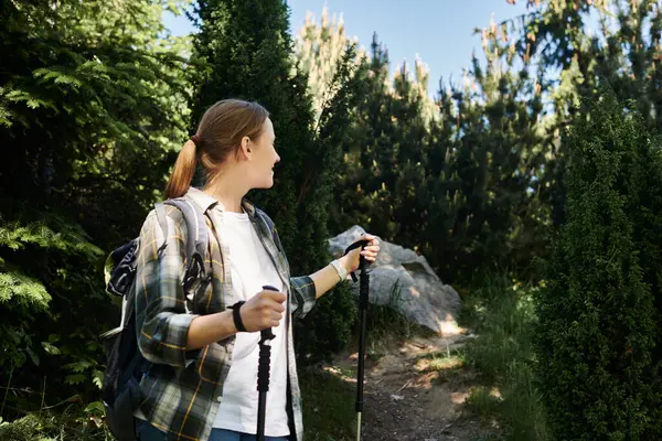 Una giovane donna cammina attraverso una lussureggiante foresta verde in una giornata estiva soleggiata, godendo l'aria fresca e la bellezza della natura.. — Foto stock