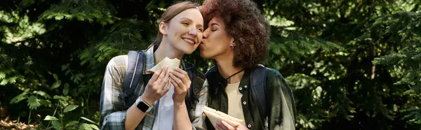 A lesbian couple enjoys a romantic hike in the woods, sharing a picnic lunch and a kiss. — Stock Photo