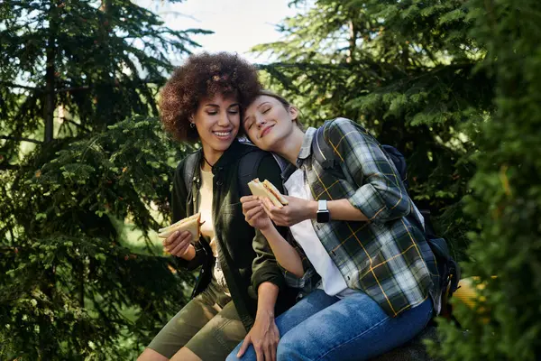 A lesbian couple enjoys a picnic lunch while hiking through a forest. — Stock Photo