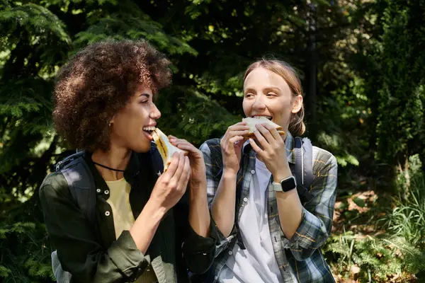 Two young women, a lesbian couple, hike together in the wilderness and enjoy a break with sandwiches. — Stock Photo