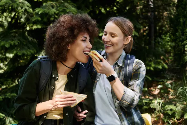 Due giovani donne, vestite con disinvoltura, si godono un pranzo al sacco mentre camminano attraverso una foresta. — Foto stock