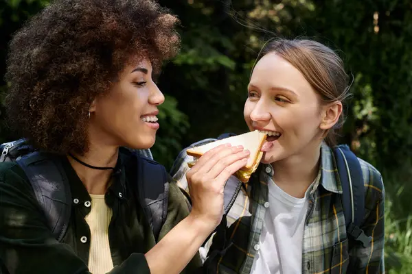 Two young women, a lesbian couple, share a sandwich on a hiking trip, enjoying the outdoors together. — Stock Photo