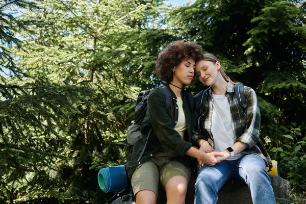 Un jeune couple de lesbiennes est assis ensemble sur un rocher dans la forêt, profitant de la paix et de la tranquillité de la nature. — Photo de stock