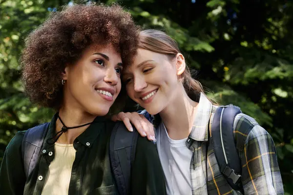 Zwei junge Frauen, eine mit lockigem braunem Haar und die andere mit glattem blonden Haar, wandern gemeinsam durch einen grünen Wald, lächeln und genießen ihre Zeit im Freien.. — Stockfoto