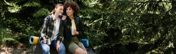 A young lesbian couple enjoys a hike in the woods, taking a break to share a drink and laugh together. — Stock Photo