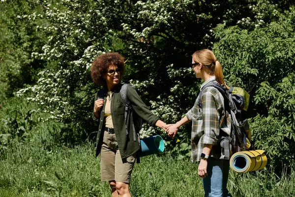 Una coppia lesbica, una nera e una bianca, cammina attraverso una lussureggiante foresta verde, godendosi il loro tempo insieme all'aria aperta. — Foto stock
