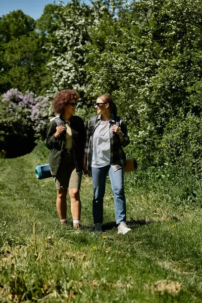 Two young women, a lesbian couple, hike together in a lush green forest on a sunny day. — Stock Photo