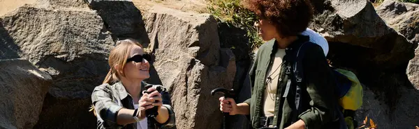 Zwei junge Frauen, eine mit blonden, die andere mit lockigen braunen Haaren, wandern gemeinsam durch die Wildnis, genießen die frische Luft und die Gesellschaft der anderen.. — Stockfoto