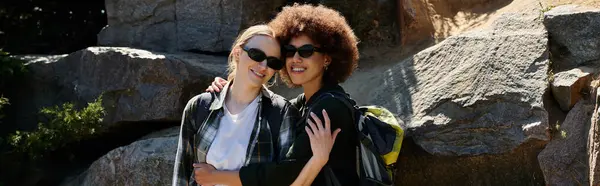 A young lesbian couple smiles for the camera while hiking through a rocky wilderness area. — Stock Photo