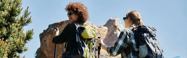 Zwei junge Frauen, eine mit brauner Haut und lockigem Haar und die andere mit heller Haut und glattem Haar, wandern gemeinsam in der Wildnis. — Stockfoto