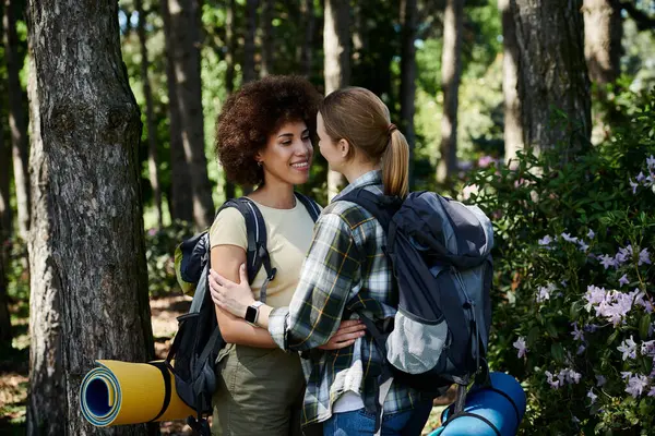 A young lesbian couple, dressed for hiking, embraces in a lush forest. — Stock Photo