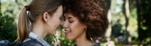 Um jovem casal lésbico, um com cabelo loiro e outro com cabelo castanho encaracolado, desfruta de uma caminhada através de uma floresta exuberante e verde. — Fotografia de Stock
