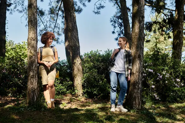 Two young women stand near trees in a forest, enjoying a hike together. — Stock Photo