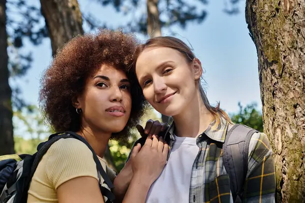 Two young women, a lesbian couple, smile for the camera during a hike in a forest. — Stock Photo