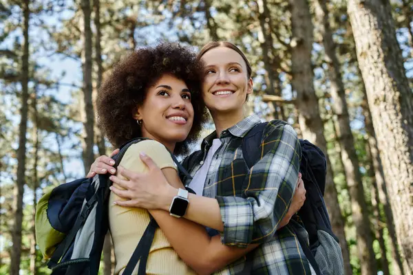 A lesbian couple smiles and embraces while hiking in the woods. — Stock Photo