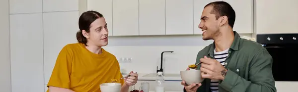 Un jeune couple gay s'assoit à un comptoir de cuisine, profitant d'un repas ensemble dans leur appartement moderne. — Photo de stock