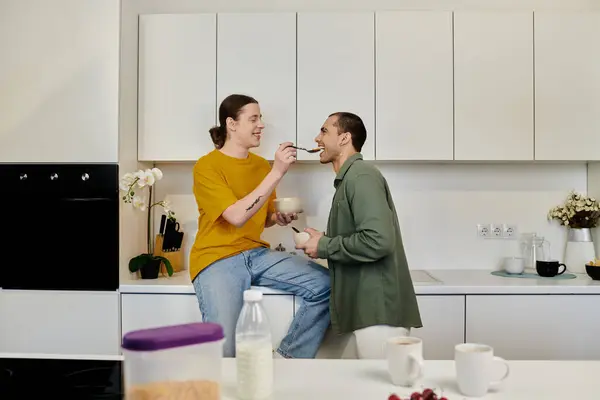 A young gay couple enjoys a playful moment in their modern kitchen, sharing breakfast and laughter. — Stock Photo