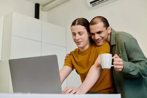 Ein junges schwules Paar verbringt viel Zeit miteinander in seiner modernen Wohnung, während der eine Partner am Laptop surft, während der andere liebevoll zuschaut. — Stockfoto