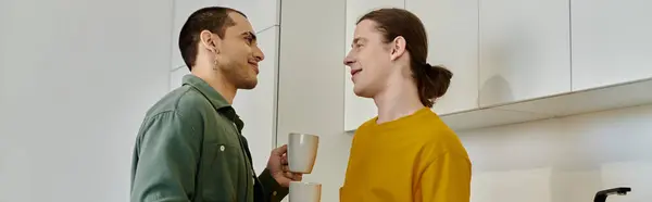 A young gay couple enjoys a casual morning together in their modern kitchen, sharing a warm drink and smiles. — Stock Photo