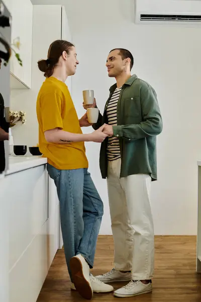 A young gay couple enjoys a cozy moment in their apartment, sharing coffee and smiles. — Stock Photo