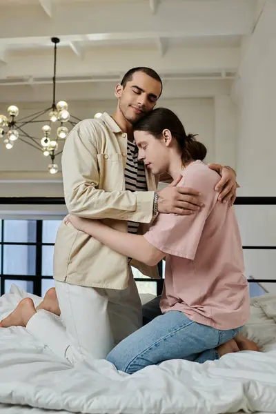 A young gay couple embraces on a white bed in their modern apartment. — Stock Photo