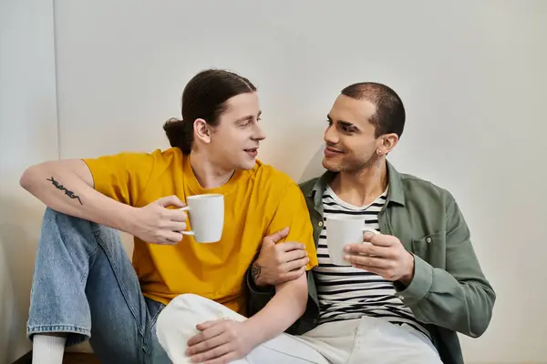 A young gay couple enjoys a relaxing morning together in their apartment, sipping coffee and sharing a tender gaze. — Stock Photo