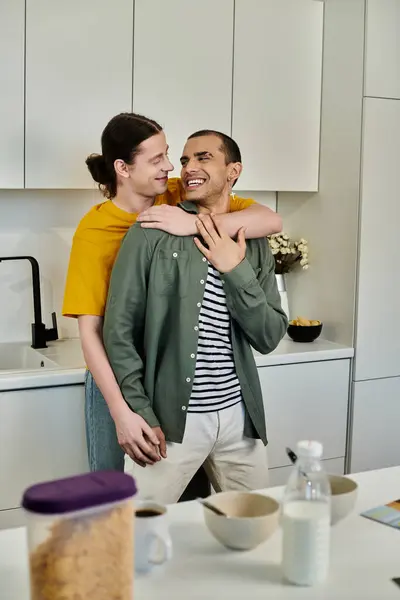 A young gay couple shares a lighthearted moment in their modern kitchen, embracing and laughing together. — Stock Photo