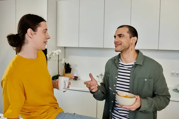 A young gay couple enjoys breakfast and conversation in their modern apartment kitchen. — Stock Photo