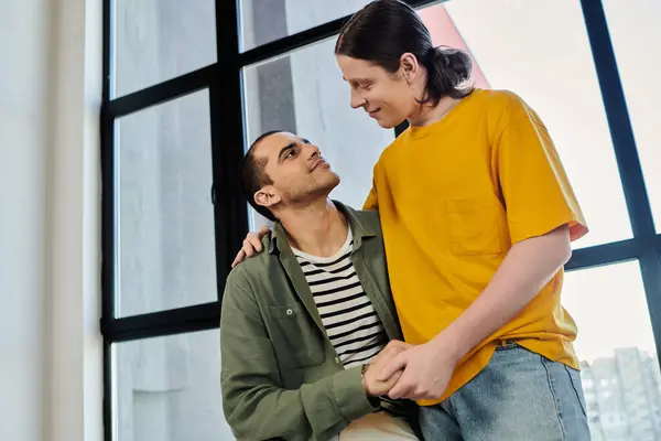 A young gay couple shares a tender moment in their modern apartment, filled with natural light. — Stock Photo