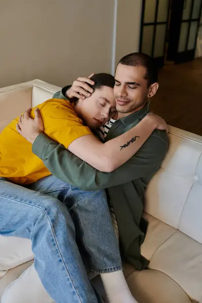 A young gay couple cuddles on a couch in a modern apartment. — Stock Photo