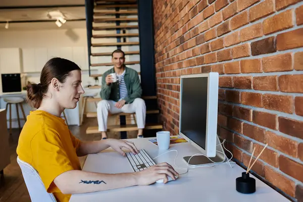 Un jeune couple gay passe un après-midi décontracté dans leur appartement moderne. Un partenaire travaille à un bureau tandis que l'autre se détend à proximité. — Photo de stock