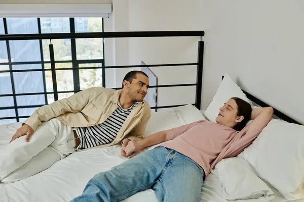 A young gay couple relaxes on a bed in a modern apartment, sharing a tender moment of connection. — Stock Photo
