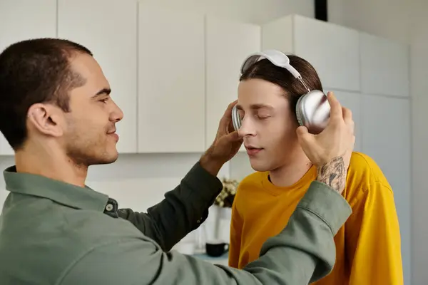 Un jeune couple gay se détend dans leur appartement moderne, l'un mettant des écouteurs sur l'autre. — Photo de stock