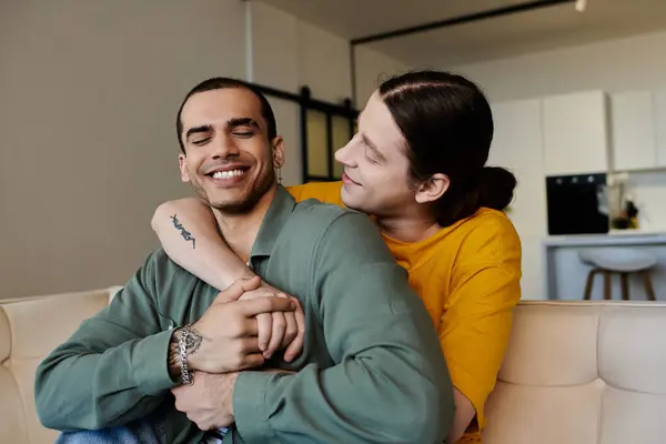 Ein junges schwules Paar in lässiger Kleidung umarmt sich liebevoll, während es auf einer Couch in seiner modernen Wohnung sitzt. — Stockfoto