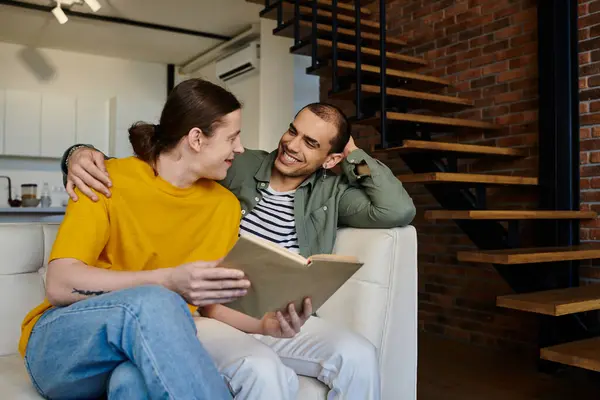 Due giovani uomini in abbigliamento casual si godono la compagnia mentre leggono un libro in un appartamento moderno. — Foto stock
