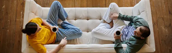 A young gay couple relaxes on a couch in their modern apartment, enjoying a casual moment together. — Stock Photo