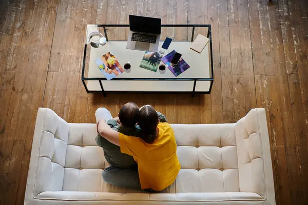Una joven pareja gay se acurruca en un sofá blanco en su apartamento moderno, disfrutando de una tarde tranquila juntos. - foto de stock