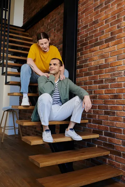 A young gay couple enjoys a moment of intimacy and comfort on the stairs of their modern apartment. — Stock Photo