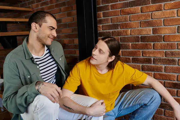 A young gay couple sits casually in their apartment, sharing a moment of intimacy. — Stock Photo