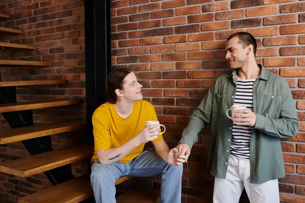 A young gay couple in casual attire enjoys a coffee break together in their modern apartment. — Stock Photo